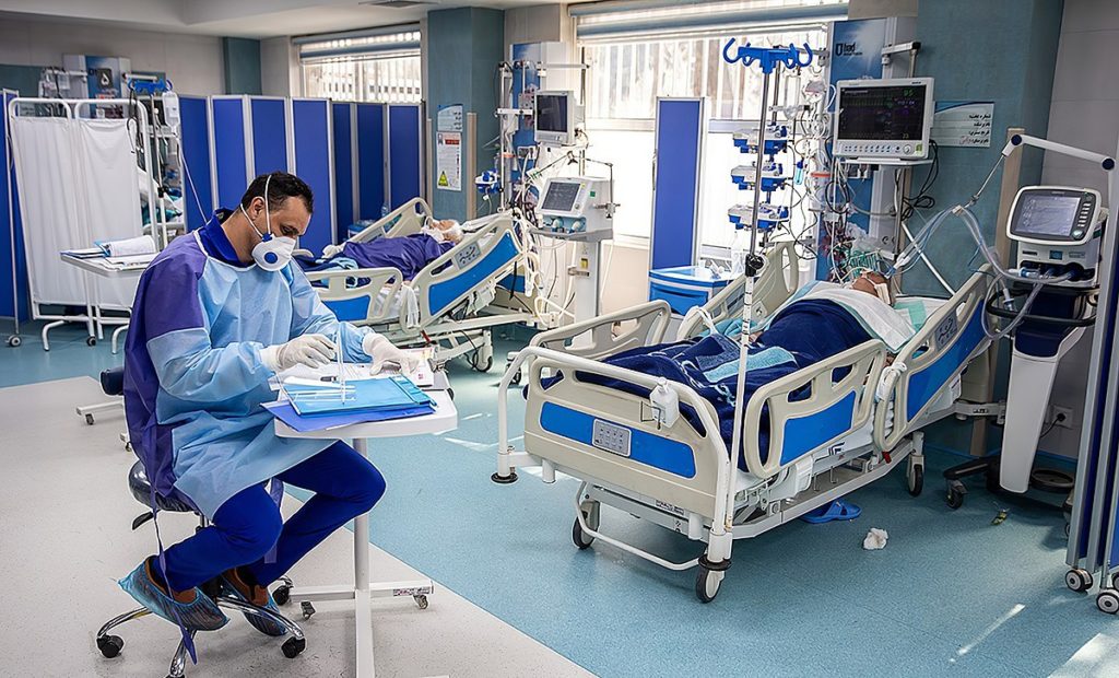 A clinician updates files in an intensive care unit in Iran surrounded by hospital beds.