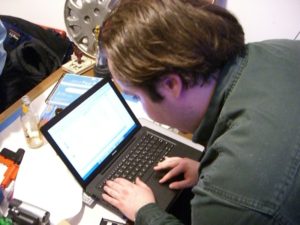 Man bending over a laptop typing on a keyboard hacking a computer